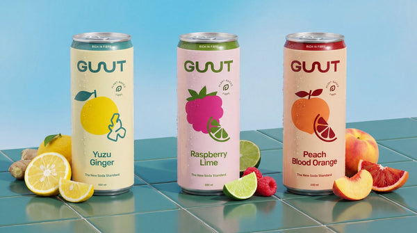 Three colourful cans of GUUTSy prebiotic soda standing together against a bright background.