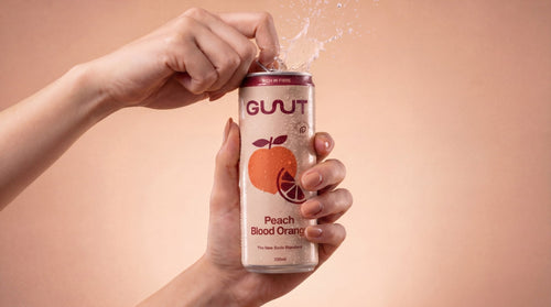 Pouring a refreshing can of GUUT Peach Blood Orange healthy sparkling soda for gut health.