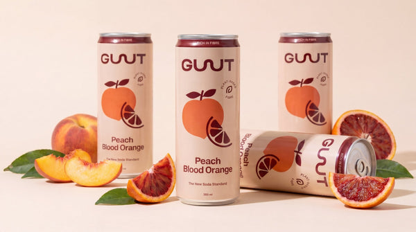A lineup of GUUT Peach Blood Orange functional fiber soda cans surrounded by fresh blood orange slices.