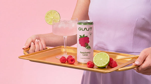 GUUT Raspberry Lime prebiotic beverage styled cleanly alongside fresh red raspberries and lime slices.