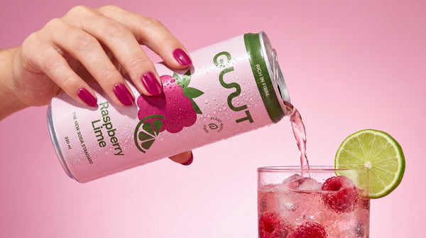 Pouring a refreshing can of GUUT Raspberry Lime healthy sparkling soda over ice with fresh lime accents.