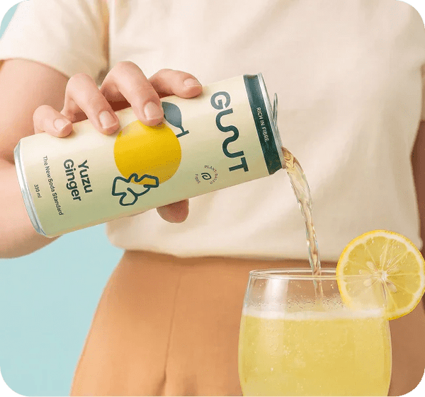Hand holding GUUT Yuzu Ginger prebiotic soda with fresh yuzu slices and ginger